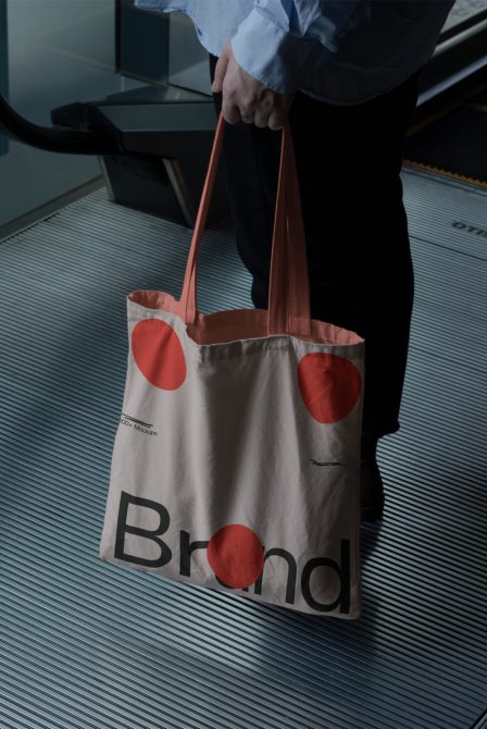 Person holding a tote bag with a brand logo, ideal for mockup design assets, showcasing brand identity on products in real-world settings.